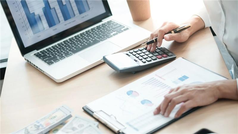 A person crunching numbers on a calculator with a laptop, documents, and cash on a desk, representing the financial challenges and paperwork owner-operators face with semi-truck financing in Ontario.