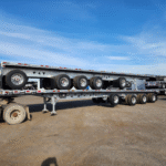 A grey flatbed semi-trailer with multiple axles parked in an outdoor lot.