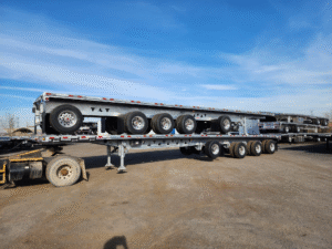 A grey flatbed semi-trailer with multiple axles parked in an outdoor lot.